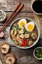 Photo of Noodle soup. Bowl of delicious ramen, ingredients and chopsticks on wooden table, flat lay