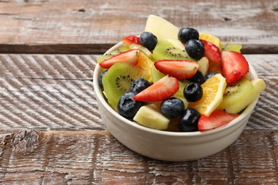 Photo of Tasty fruit salad in bowl on wooden table, closeup. Space for text