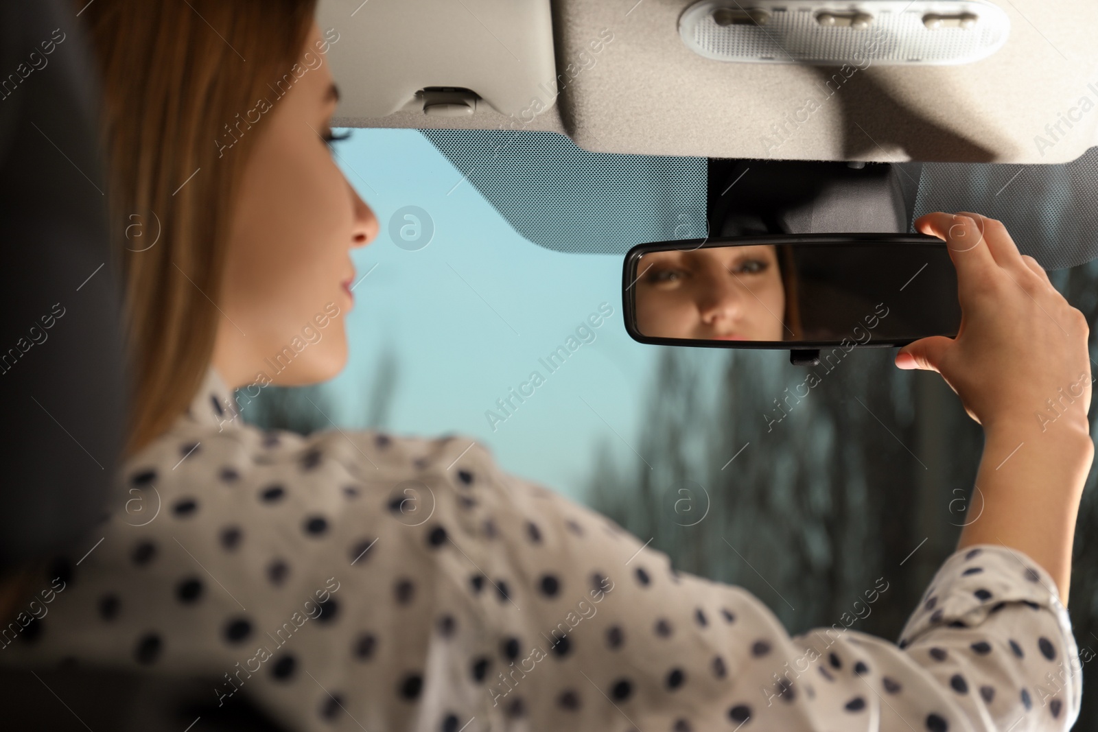 Photo of Young woman adjusting rear view mirror in car, closeup