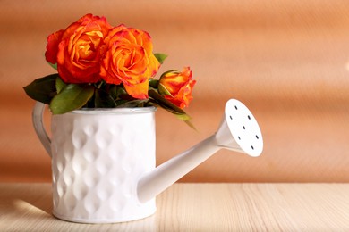 Stylish watering can with beautiful orange roses on white wooden table