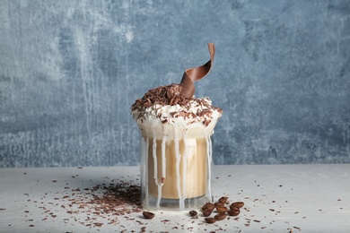 Photo of Glass cup of tasty coffee with whipped cream and chocolate on table against color background