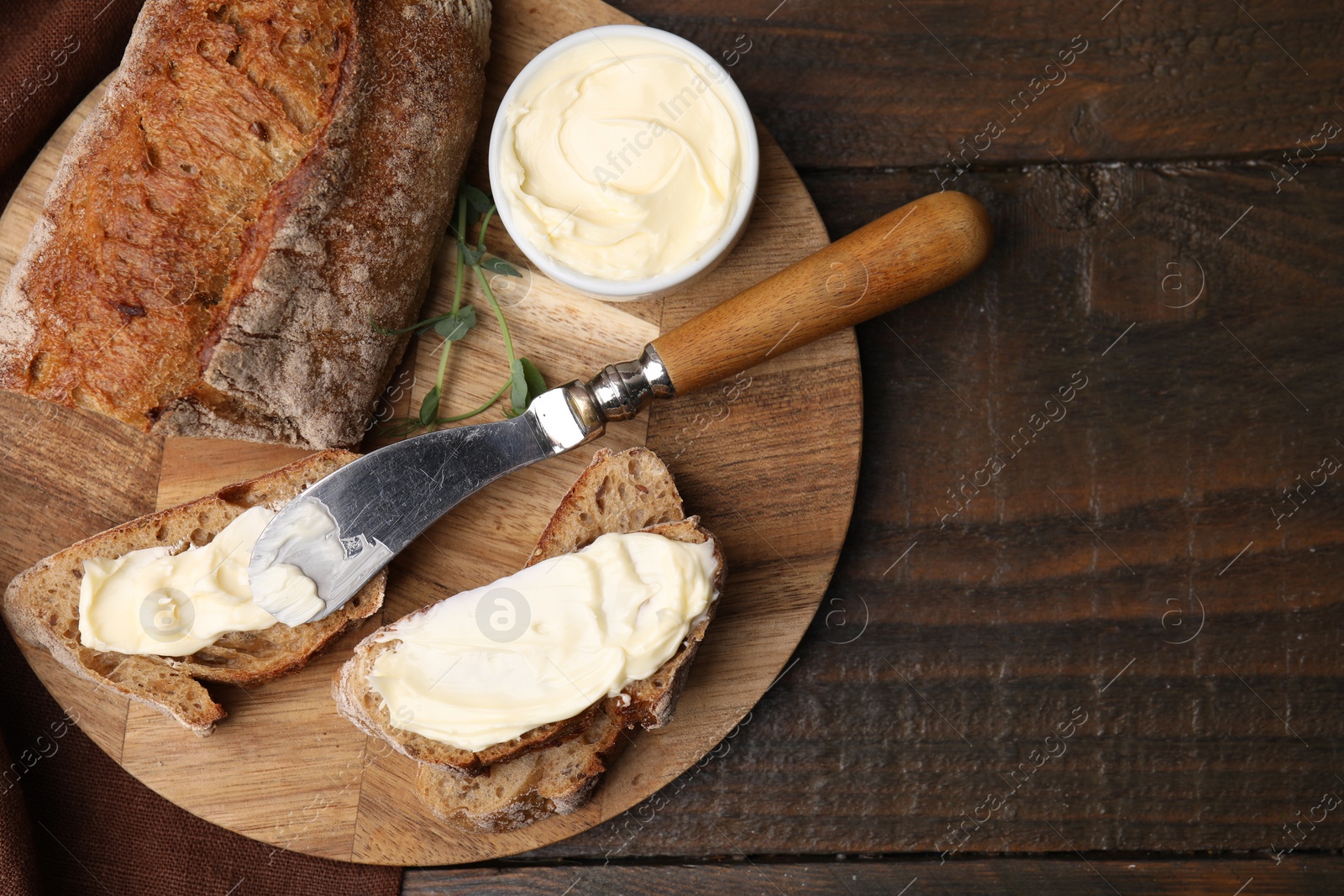 Photo of Tasty bread with butter and knife on wooden table, top view. Space for text
