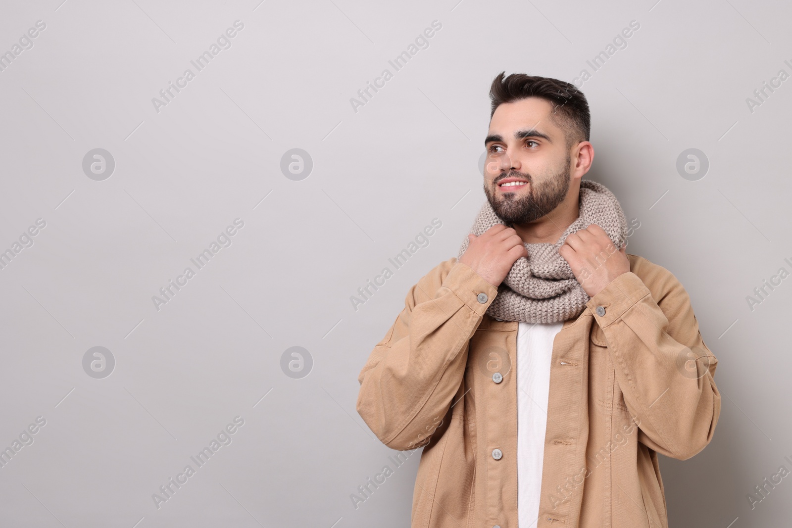 Photo of Smiling man in warm scarf on light grey background. Space for text