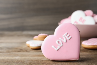 Heart shaped cookie with word Love on wooden table, closeup and space for text. Valentine's day treat