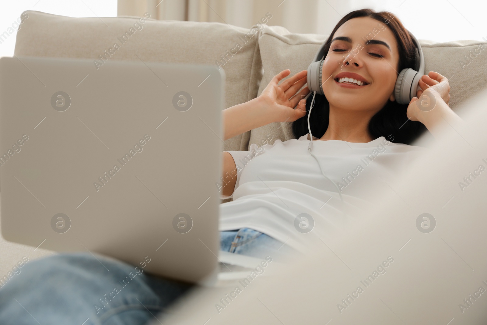 Photo of Woman with laptop and headphones lying on sofa at home