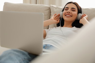 Woman with laptop and headphones lying on sofa at home