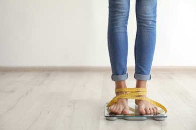Photo of Woman with tape measuring her weight using scales on wooden floor. Healthy diet