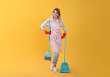Photo of Young housewife with broom and dustpan on yellow background