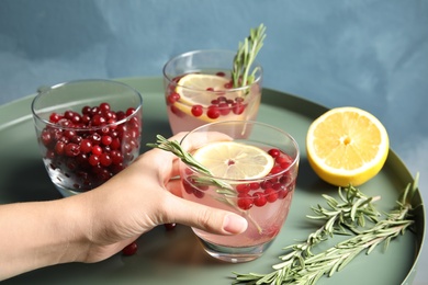 Woman holding glass of cranberry cocktail with rosemary on table