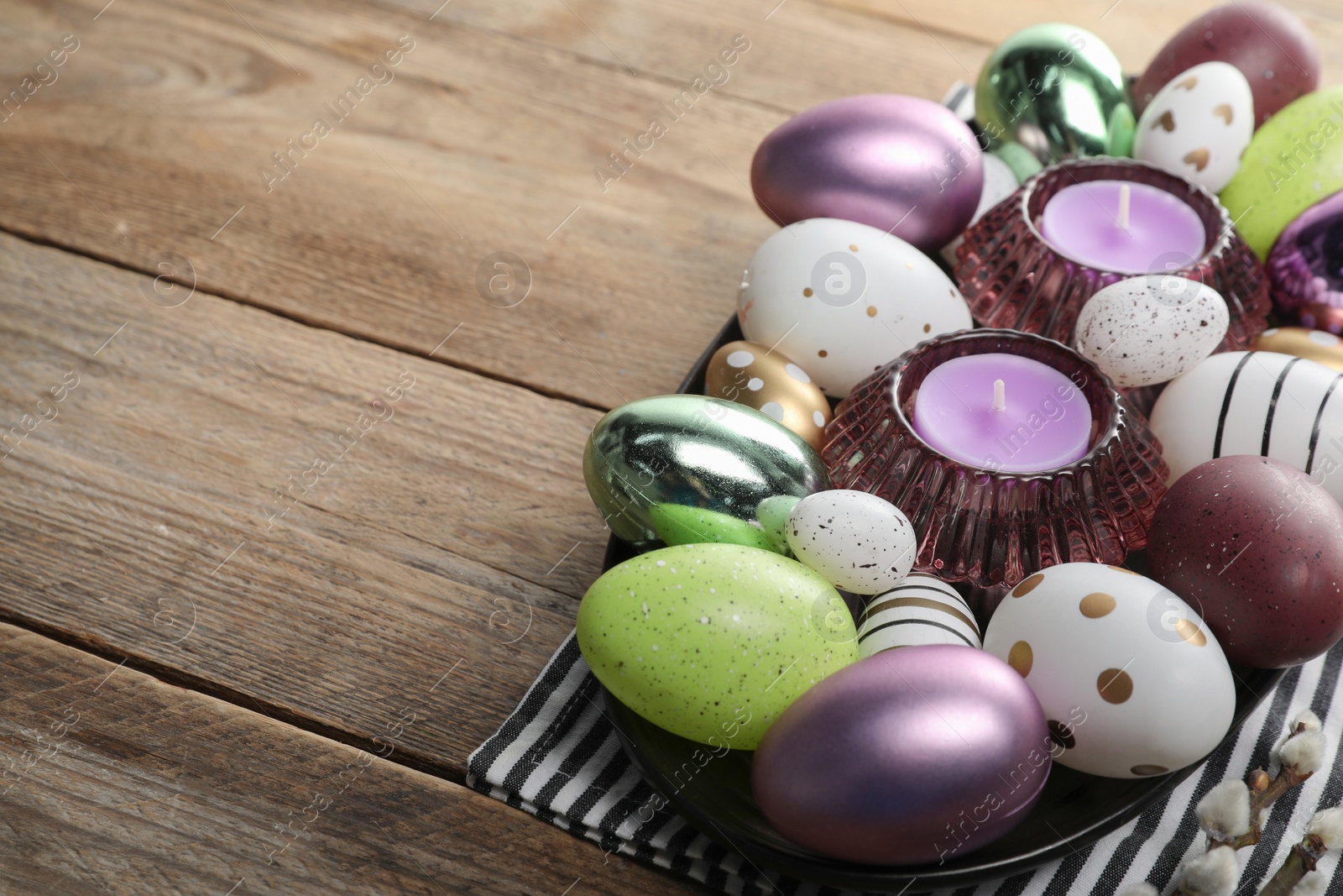 Photo of Many beautifully decorated Easter eggs and scented candles on wooden table, space for text