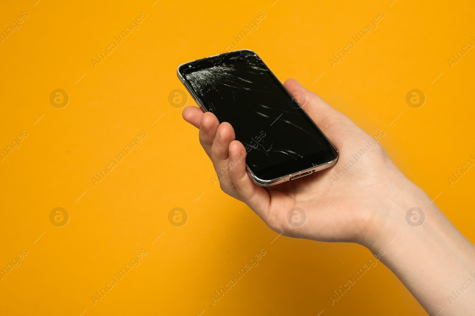 Photo of Woman holding damaged smartphone on orange background, closeup. Device repairing