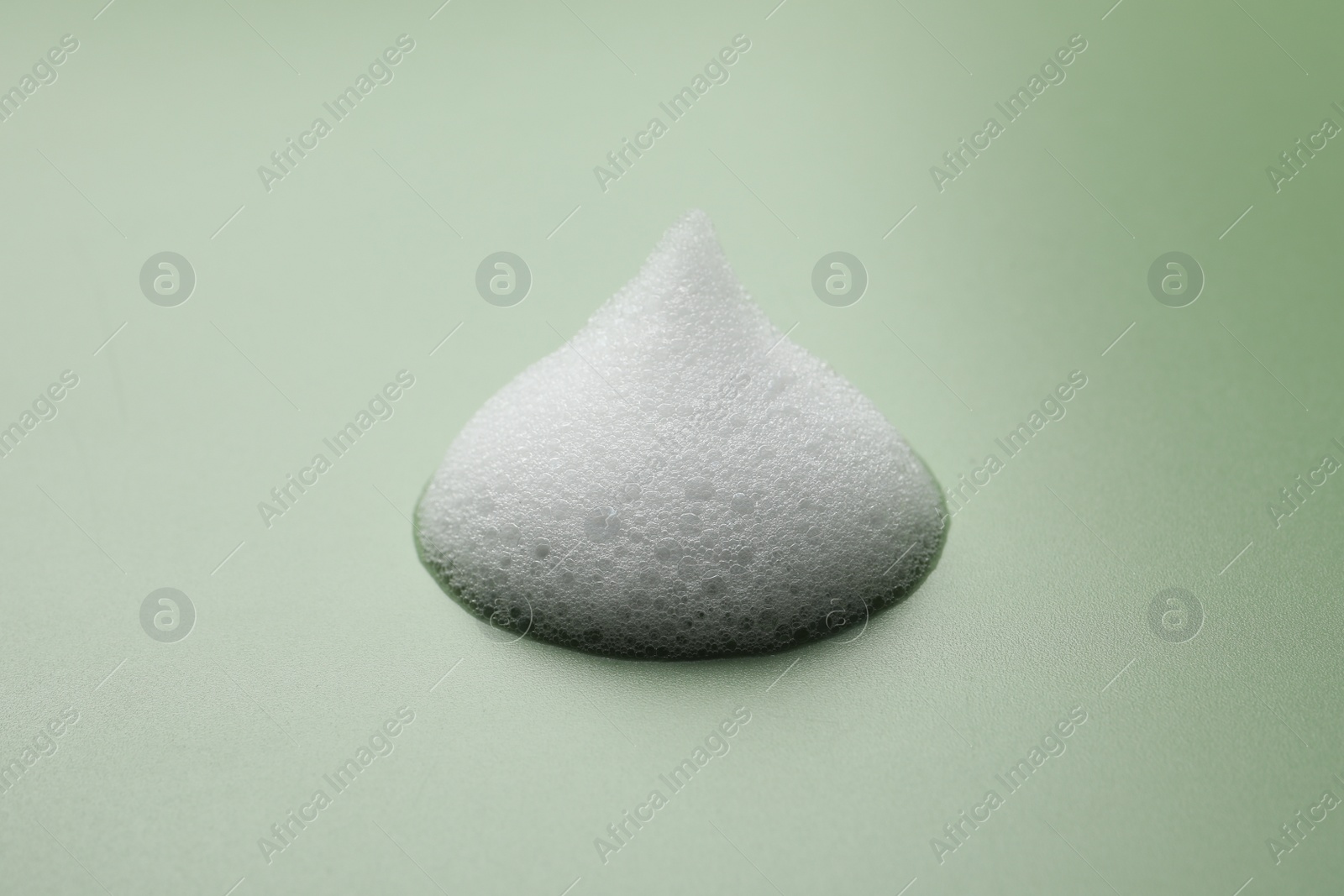 Photo of Drop of fluffy soap foam on green background