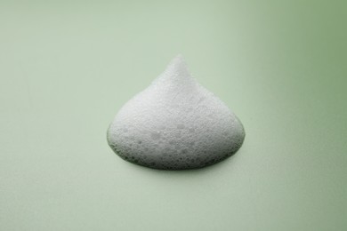 Photo of Drop of fluffy soap foam on green background