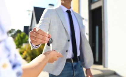 Real estate agent giving house keys to young woman outdoors, closeup