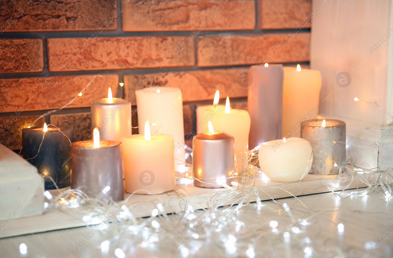 Photo of Christmas lights near decorative fireplace with candles indoors