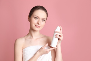 Young woman with bottle of thermal water on color background, space for text. Cosmetic product