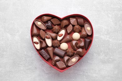 Heart shaped box with delicious chocolate candies on light grey table, top view