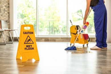 Safety sign with phrase Caution wet floor and cleaner indoors. Cleaning service