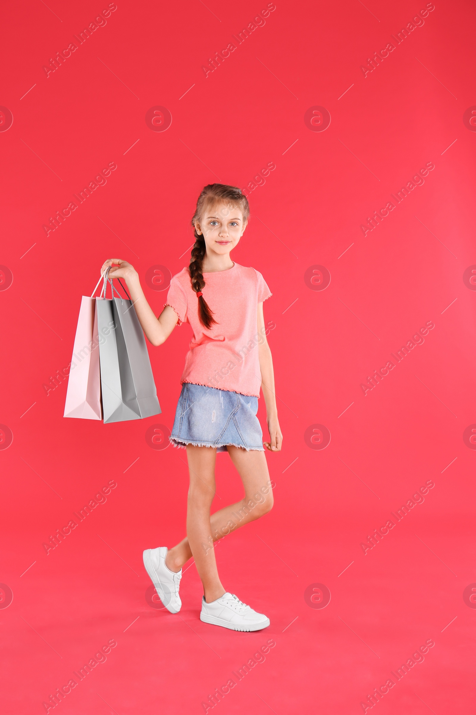 Photo of Cute little girl with shopping bags on red background