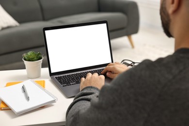 E-learning. Young man using laptop at white table indoors, closeup