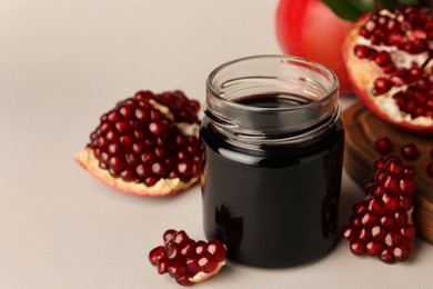 Photo of Glass jar of tasty pomegranate sauce and fresh ripe fruits on white background. Space for text