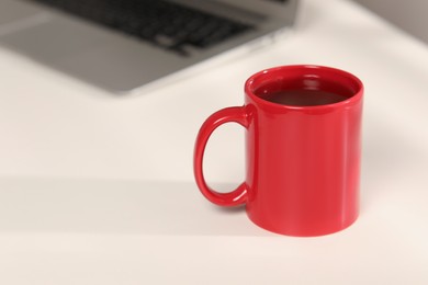 Red ceramic mug on table at workplace, space for text