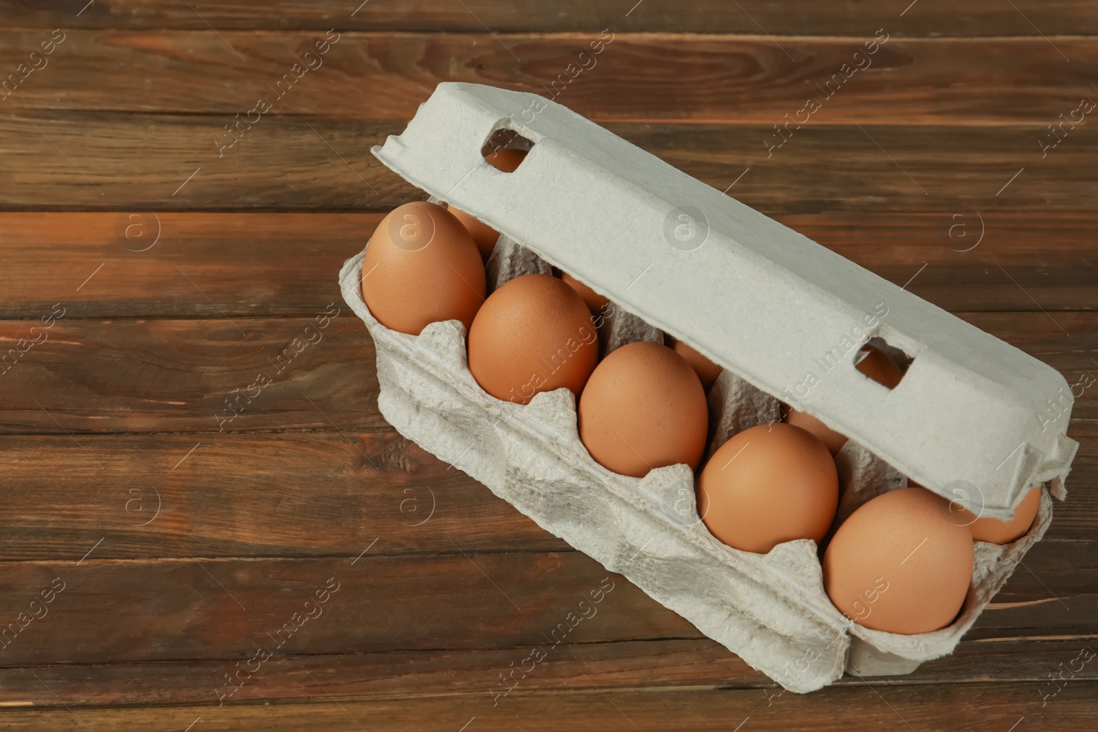 Photo of Raw chicken eggs in carton on wooden table