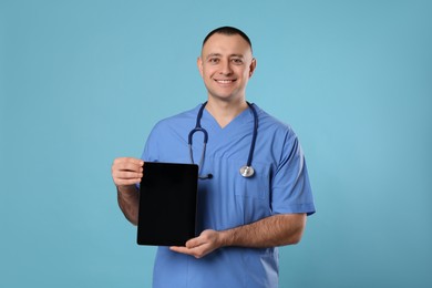 Doctor with stethoscope holding blank tablet on light blue background, space for design. Cardiology concept