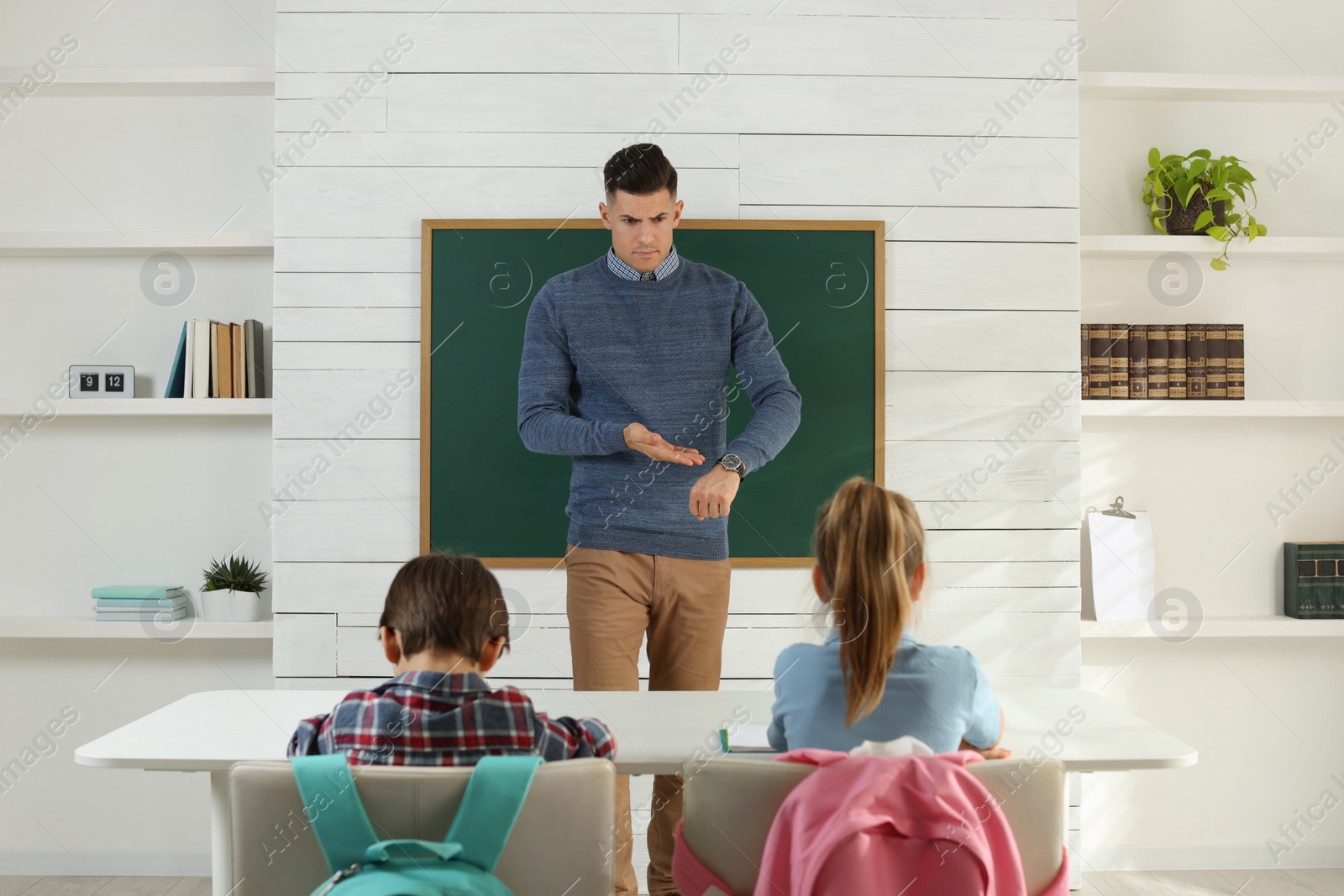 Photo of Teacher pointing on wrist watch while scolding pupils for being late in classroom