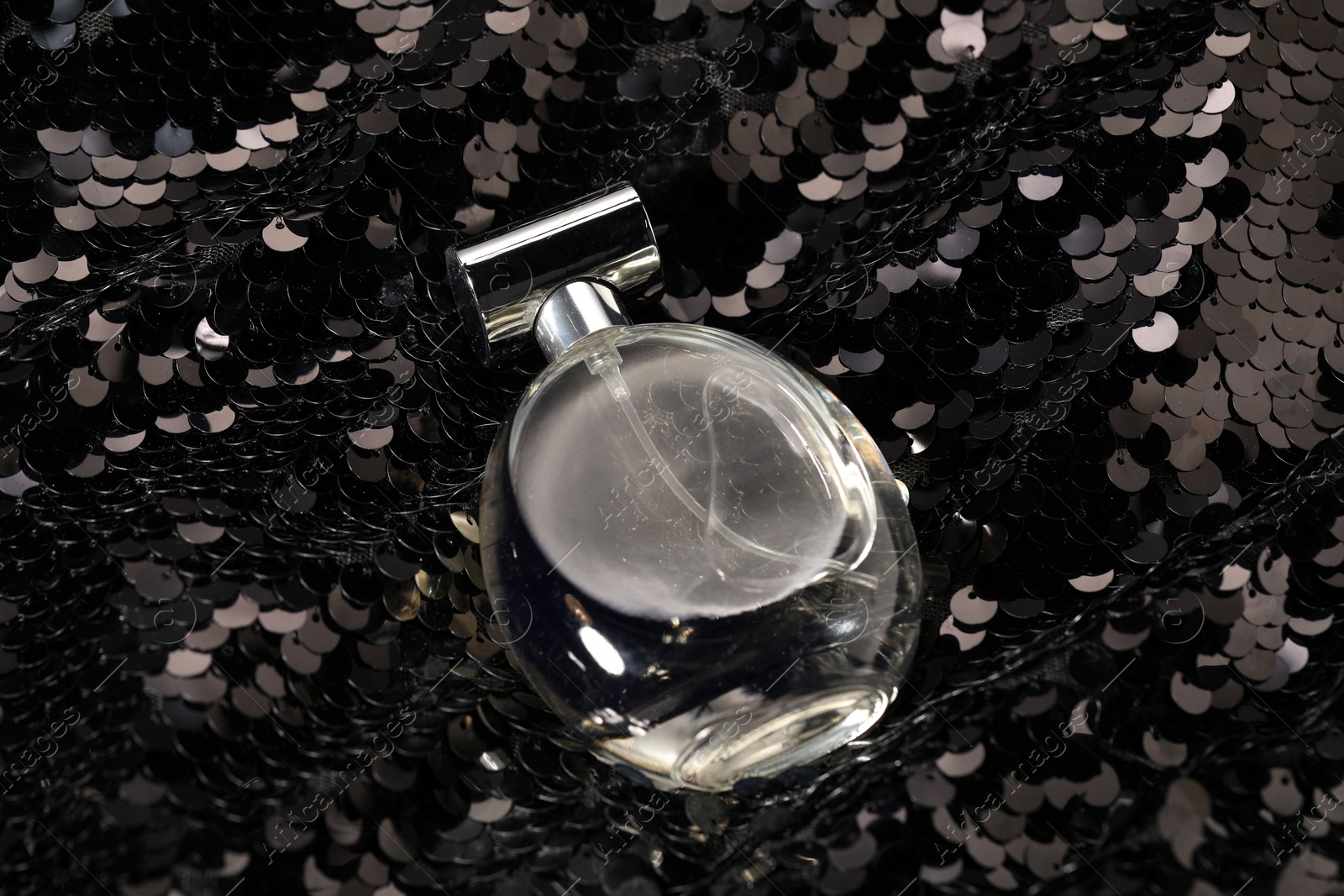 Photo of Luxury perfume in bottle on fabric with shiny sequins