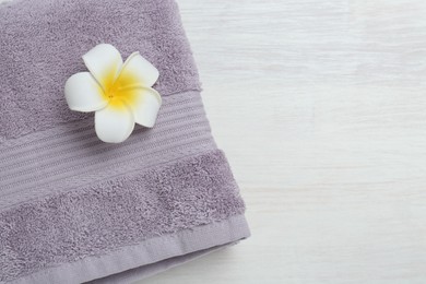 Photo of Violet terry towel and plumeria flower on light wooden table, top view. Space for text