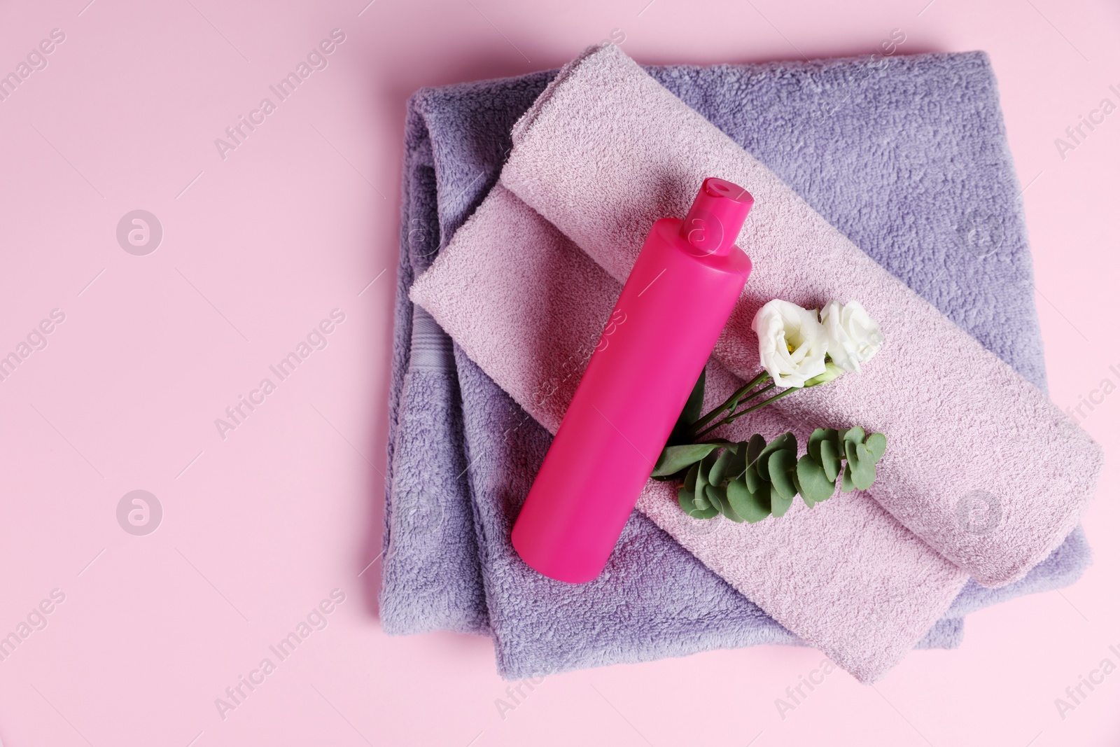 Photo of Soft folded towels with flowers, eucalyptus branch and cosmetic product on pink background, top view. Space for text