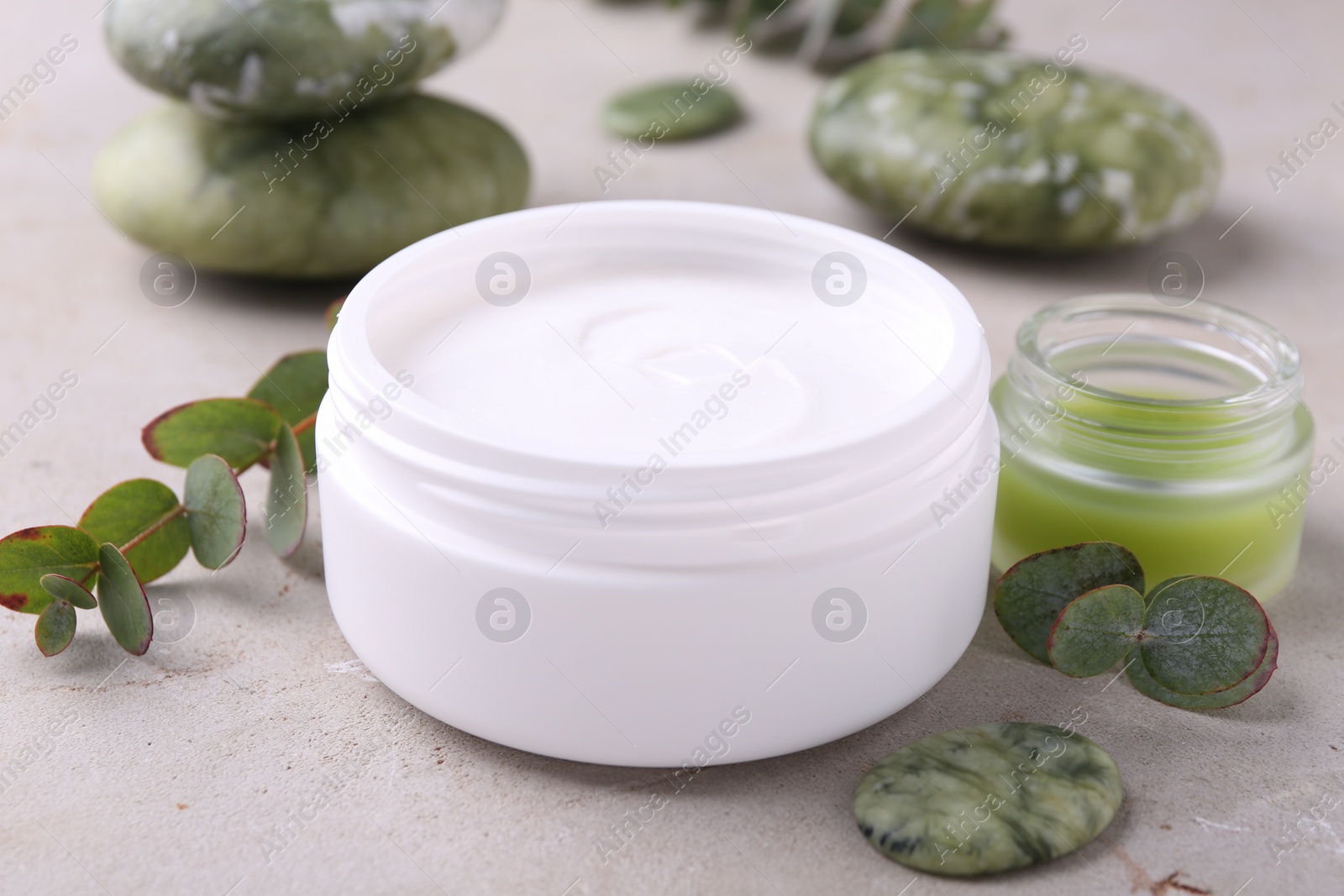 Photo of Jars of cream, spa stone and green leaves on light textured table. Body care products