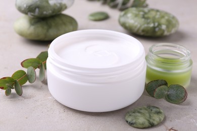 Jars of cream, spa stone and green leaves on light textured table. Body care products