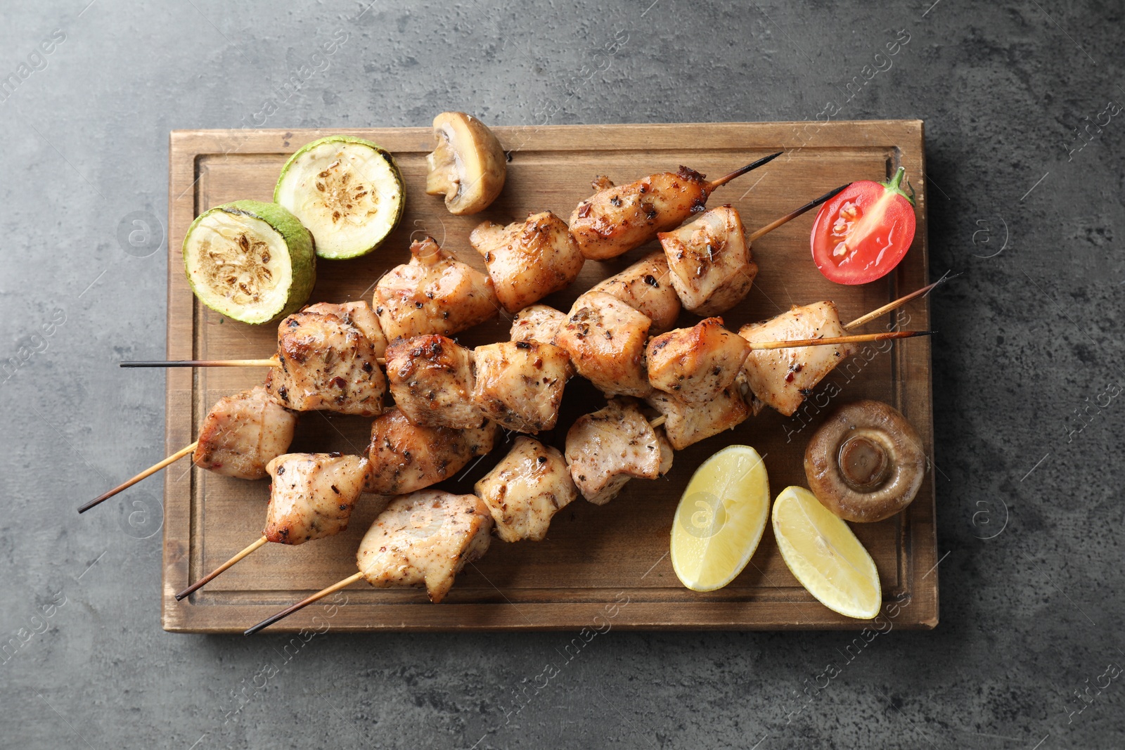 Photo of Delicious shish kebabs with vegetables and lemon on grey table, top view