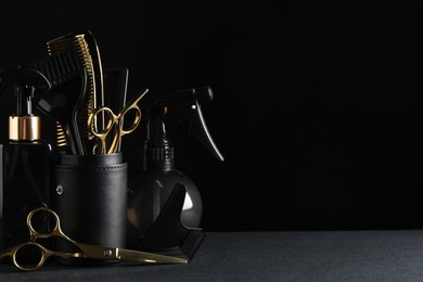 Photo of Different hairdresser tools on grey table against black background. Space for text