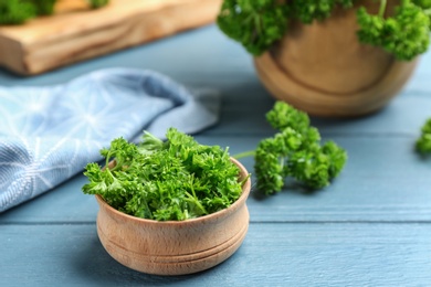Photo of Fresh curly parsley in wooden bowl on blue table