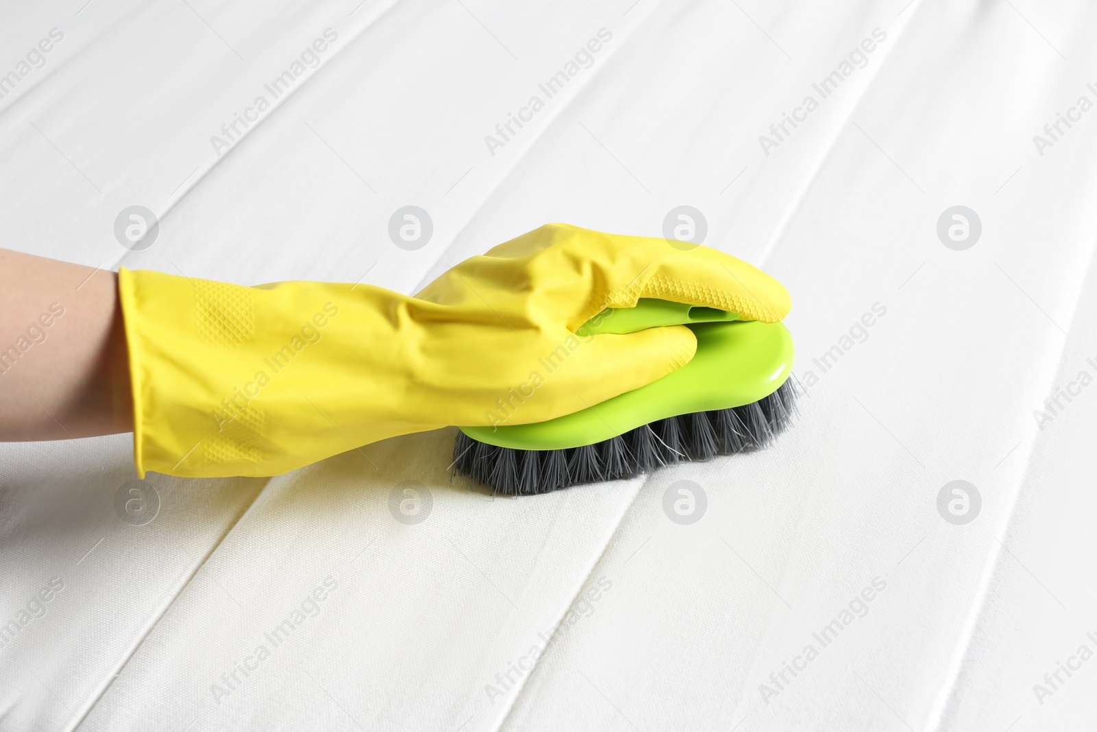 Photo of Woman in yellow gloves cleaning white mattress with brush, closeup