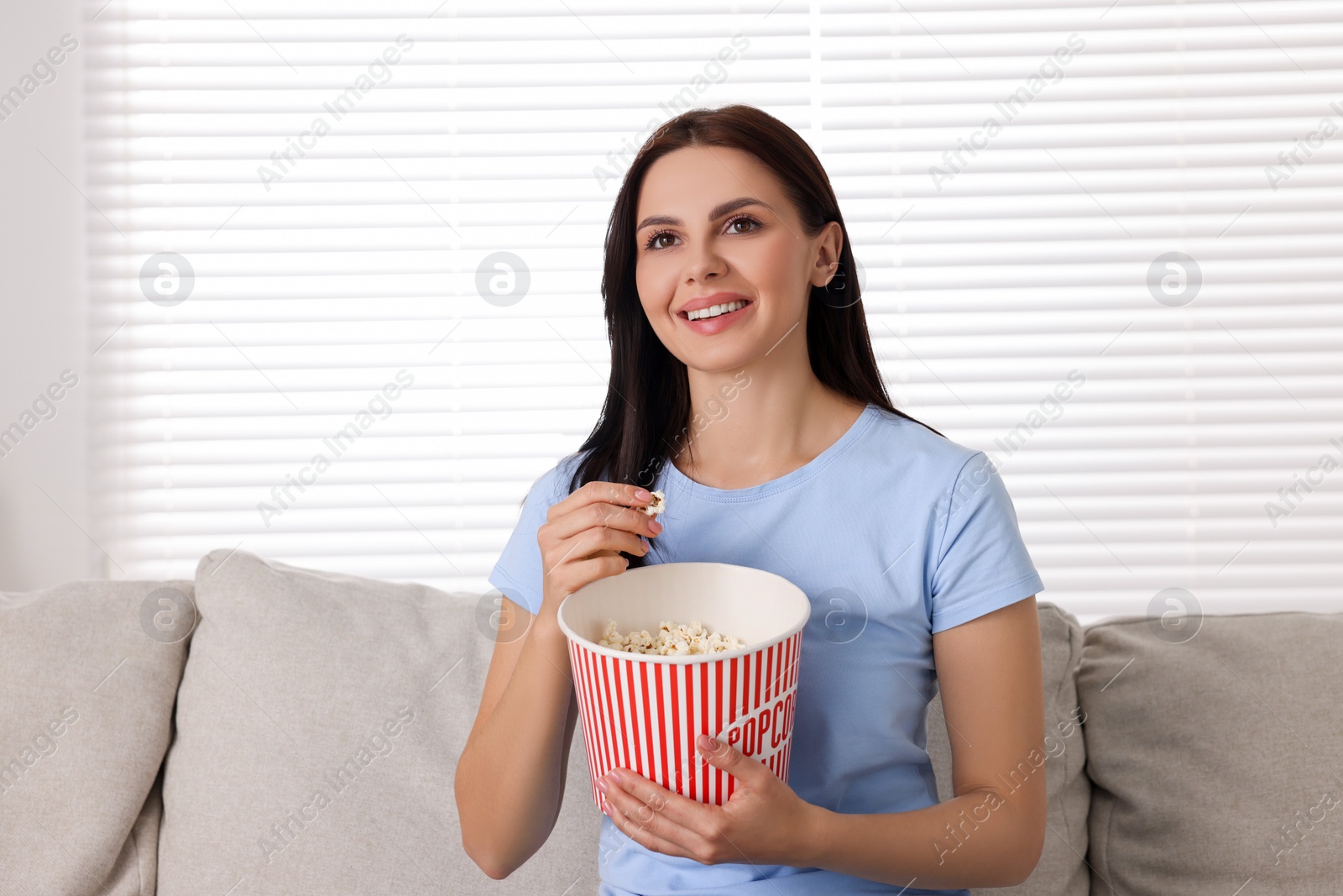 Photo of Happy woman with popcorn bucket watching TV on sofa at home