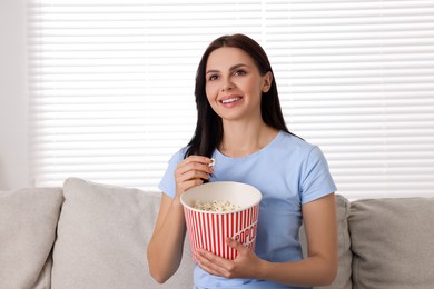 Photo of Happy woman with popcorn bucket watching TV on sofa at home