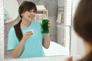 Photo of Young woman using mouthwash near mirror in bathroom