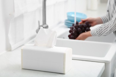 Photo of Woman washing grapes with running water over sink in kitchen, focus on paper towels. Space for text