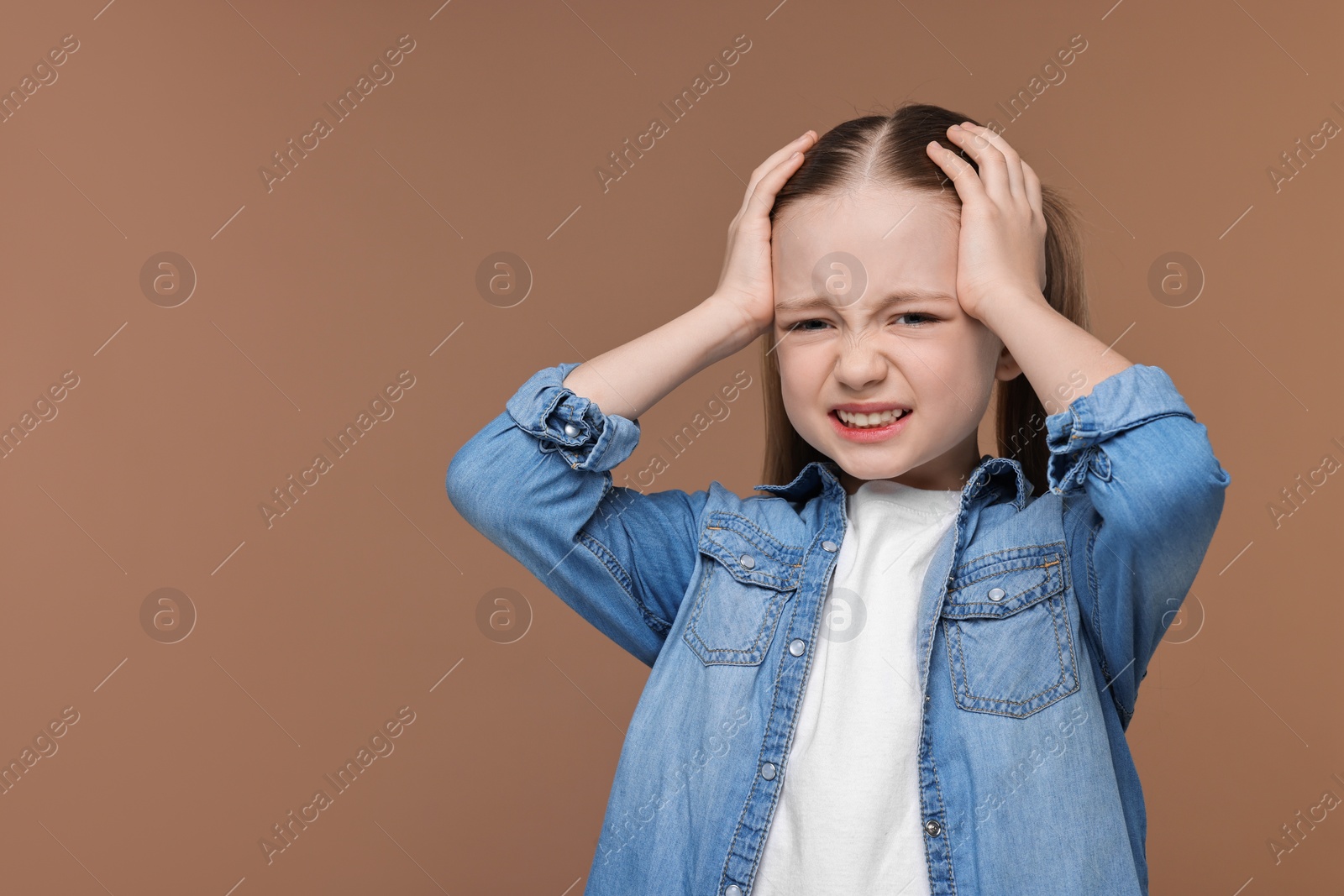 Photo of Little girl suffering from headache on brown background. Space for text