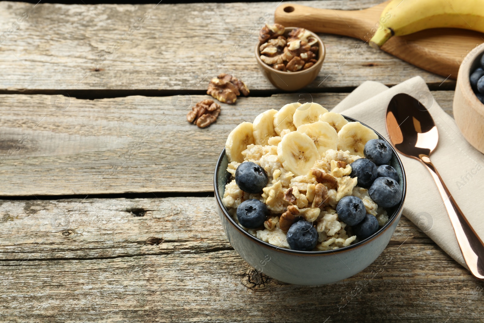 Photo of Tasty oatmeal with banana, blueberries and walnuts served in bowl on wooden table, space for text