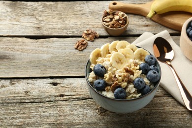 Tasty oatmeal with banana, blueberries and walnuts served in bowl on wooden table, space for text