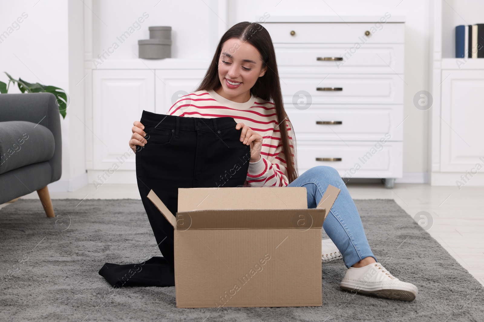 Photo of Happy young woman taking black jeans out of box at home. Online shopping