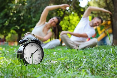 Photo of Man and woman doing morning exercise in park, focus on alarm clock