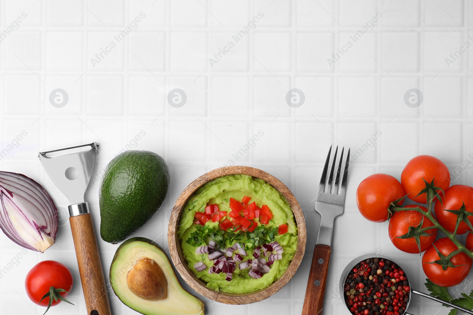 Photo of Bowl of delicious guacamole with onion, tomatoes and ingredients on white tiled table, flat lay. Space for text