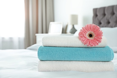 Photo of Stack of clean towels with flower on bed indoors. Space for text