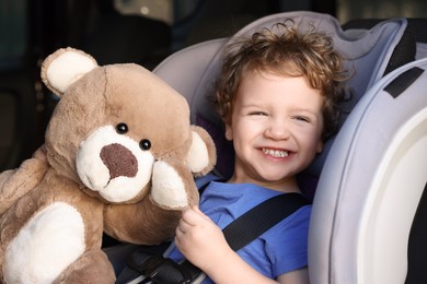 Photo of Cute little boy with teddy bear sitting in child safety seat inside car